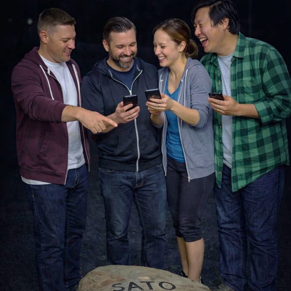 Team of players collaborating with smartphones while solving a puzzle in the Sato Code outdoor escape game